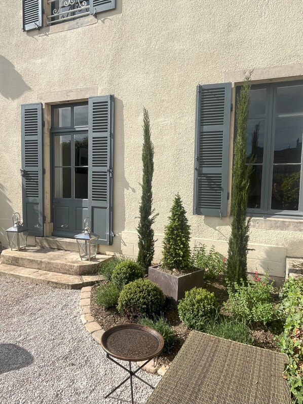 A building with a textured facade, a door with shutters, and a small outdoor seating area with a table and chairs.