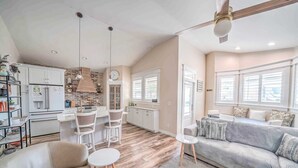 Un amplio salón con sofá, una mesa de comedor y sillas. Incluye una zona de cocina con refrigerador, estufa e iluminación colgante.