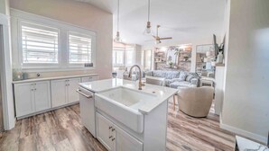Una cocina moderna con una isla central, armarios blancos y un ventanal con persianas.