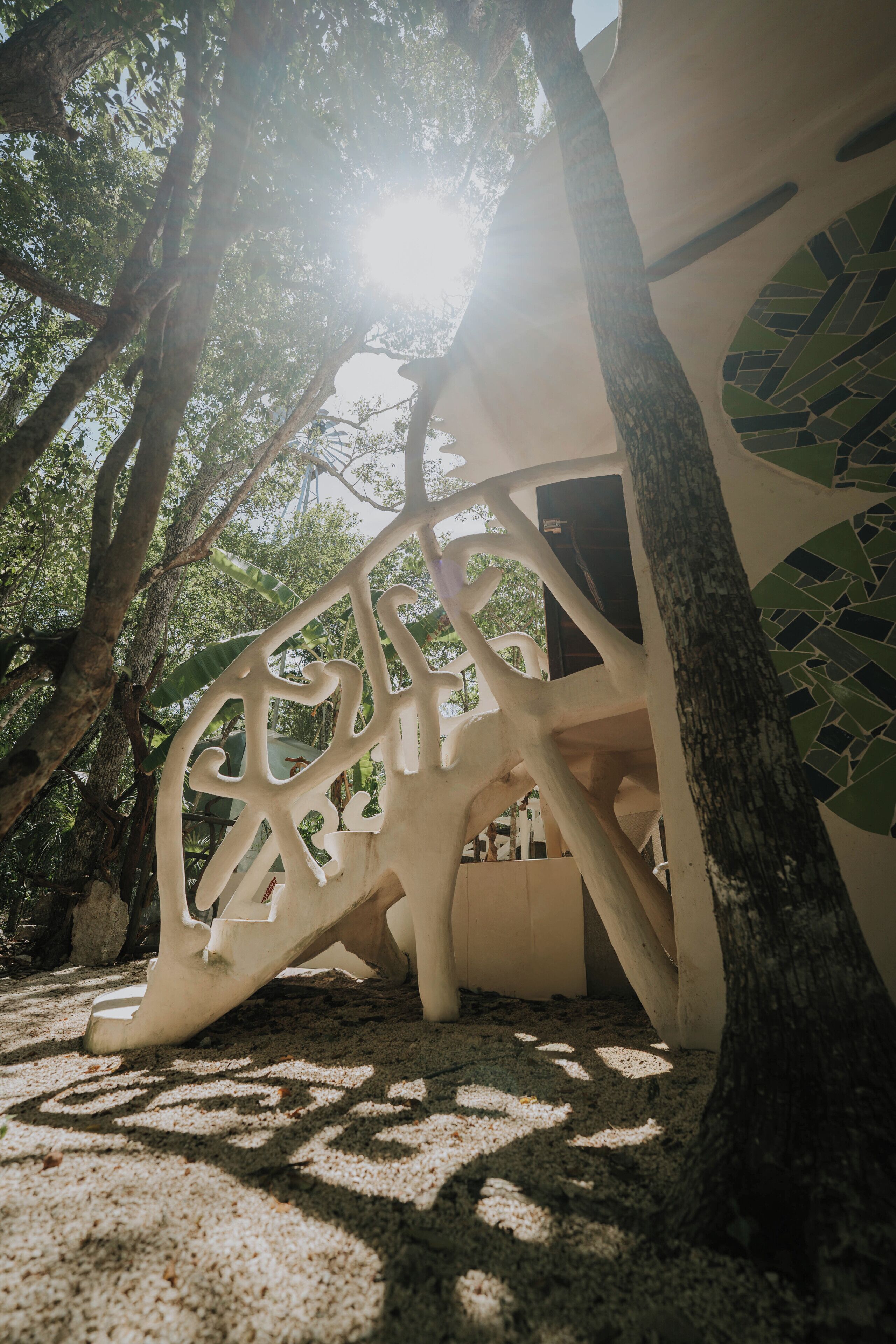 Una estructura blanca al aire libre con un diseño singular, rodeada de árboles y luz solar.