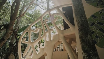 Una estructura blanca al aire libre con un diseño singular, rodeada de árboles y luz solar.
