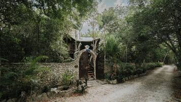 A rustic stone pathway leading to a wooden gate with a decorative archway, surrounded by lush greenery.
