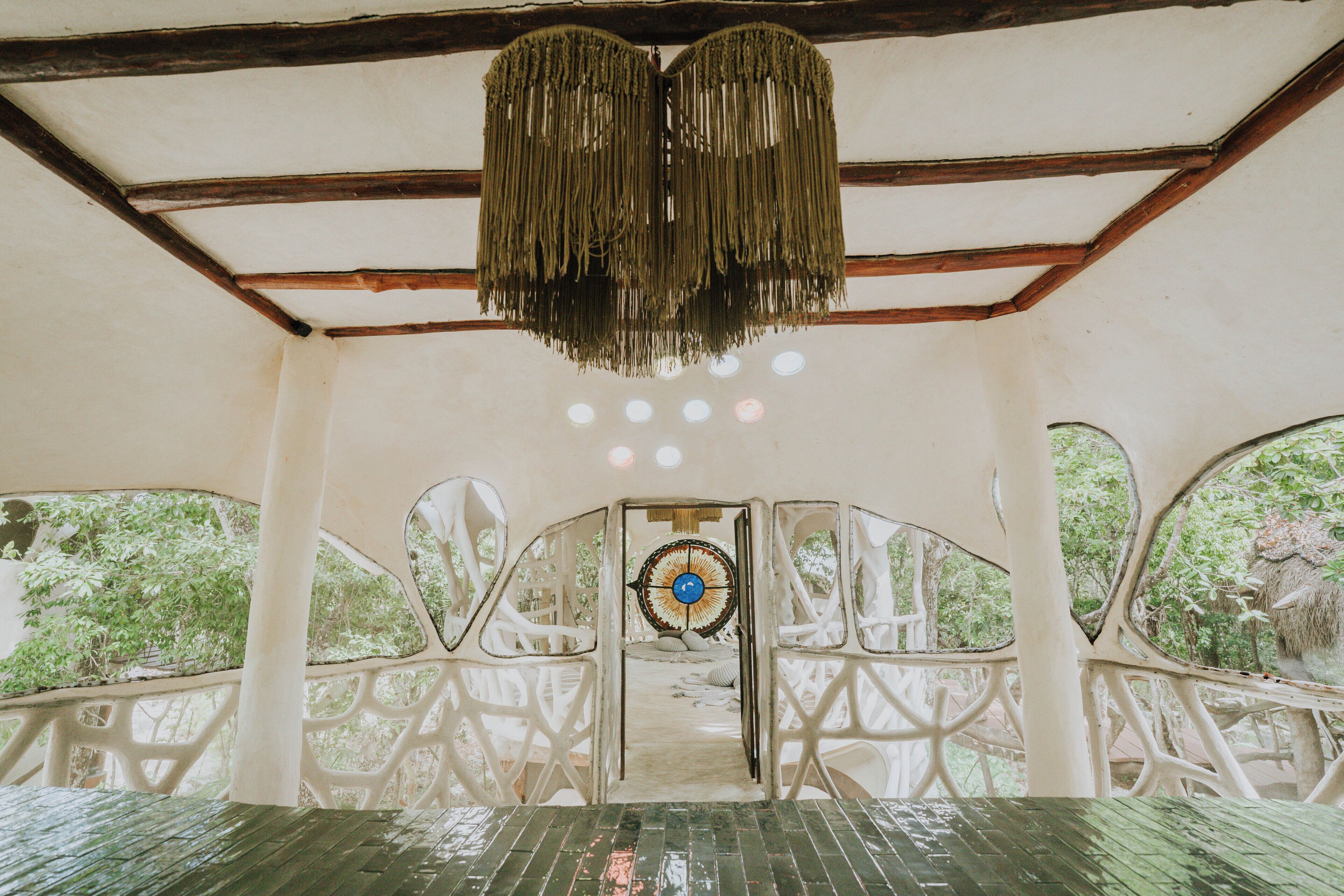 An interior with a wooden ceiling, a central door with a circular design, and a view of greenery outside.