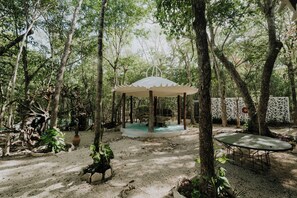 Un gazebo in una zona boschiva con tavolo e sedie sotto.