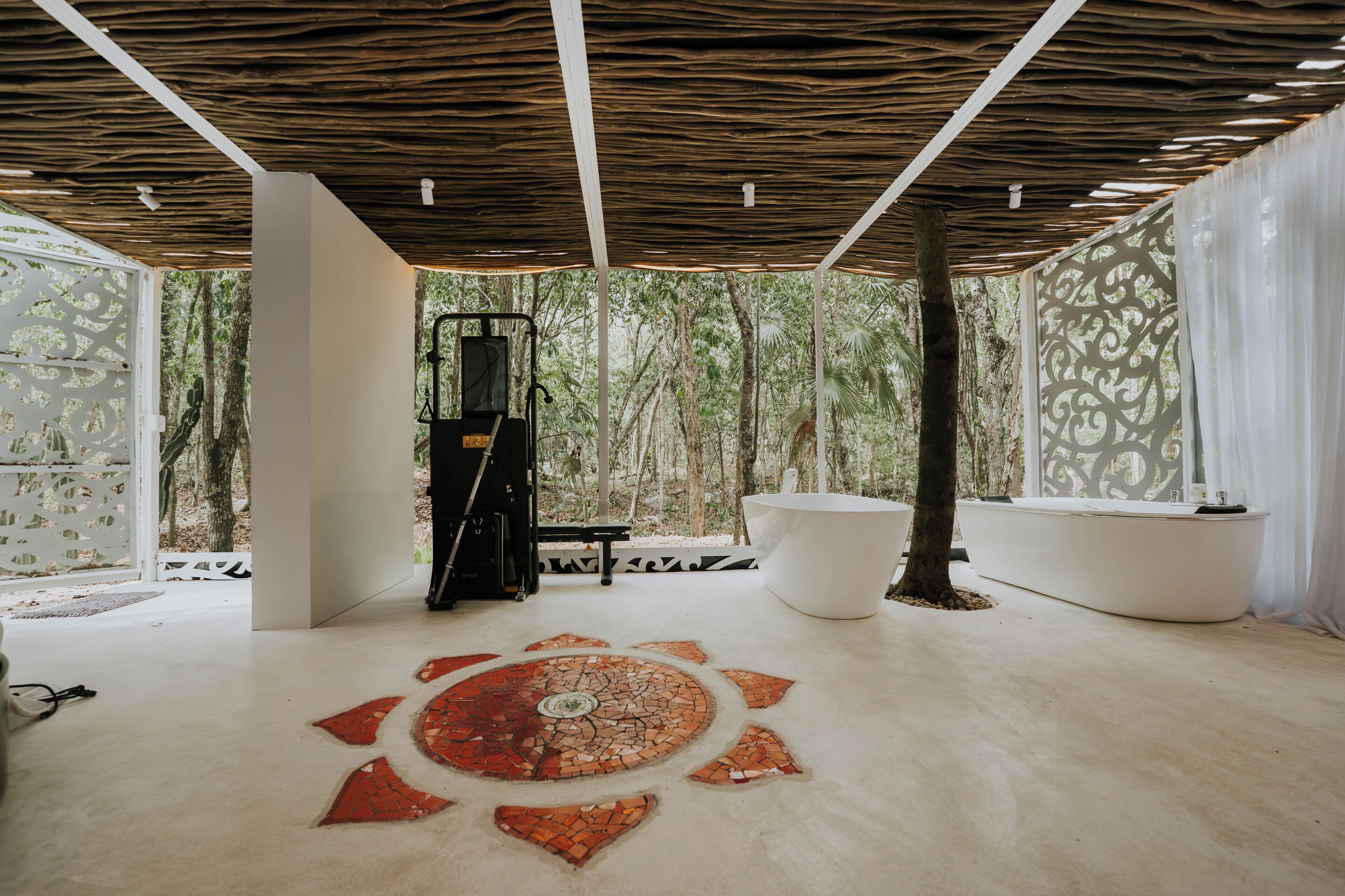 Un moderno espacio de spa con un amplio diseño de mosaico circular en el suelo, una camilla de masaje negra y una bañera blanca.
