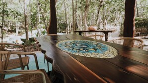 An outdoor wooden table with a mosaic centerpiece, surrounded by wicker chairs, set in a forested area. - El Sueño Riviera Maya (Tulum)