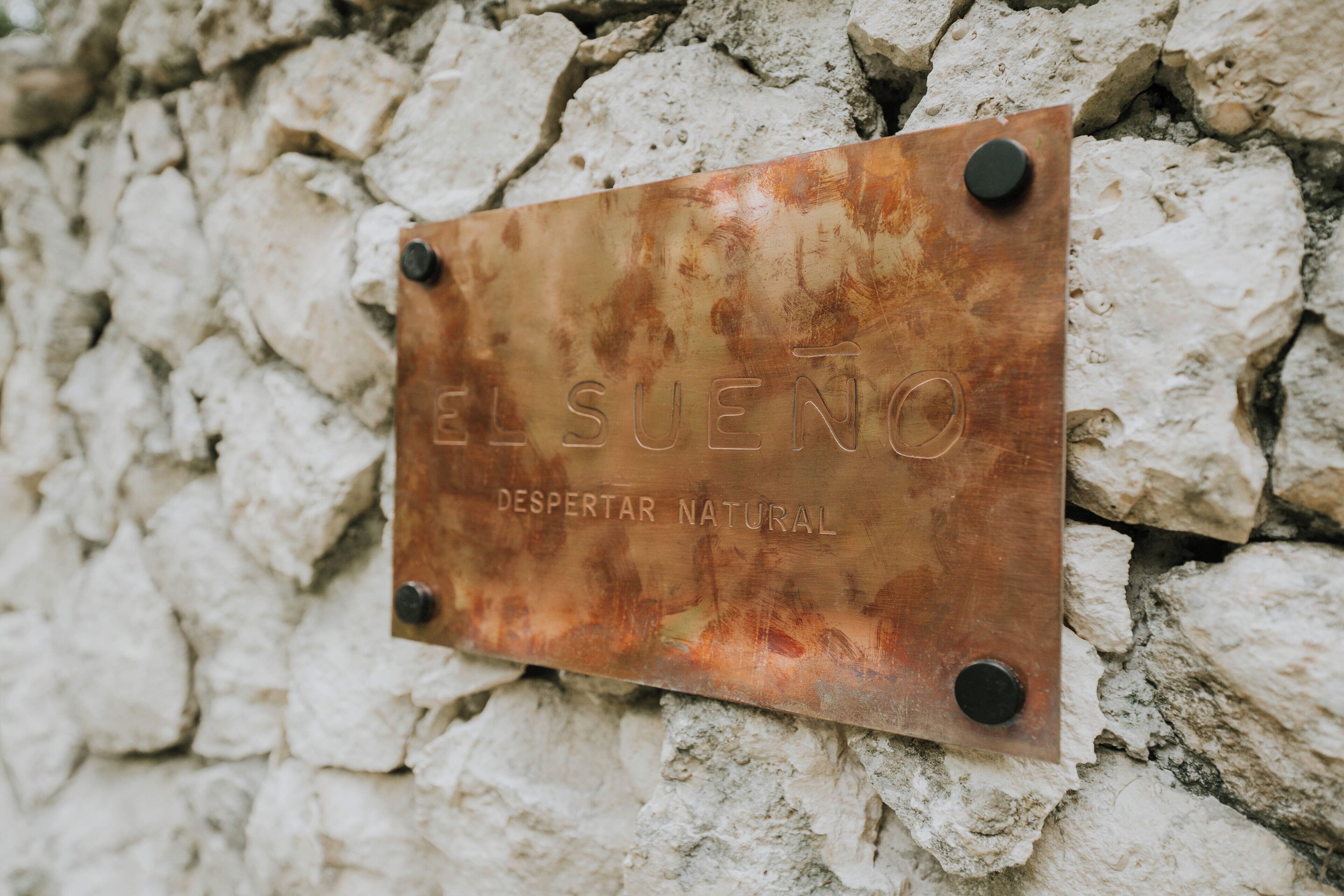 A metal plaque with the inscription 'EL SUENO DESPERTAR NATURAL' mounted on a stone wall.