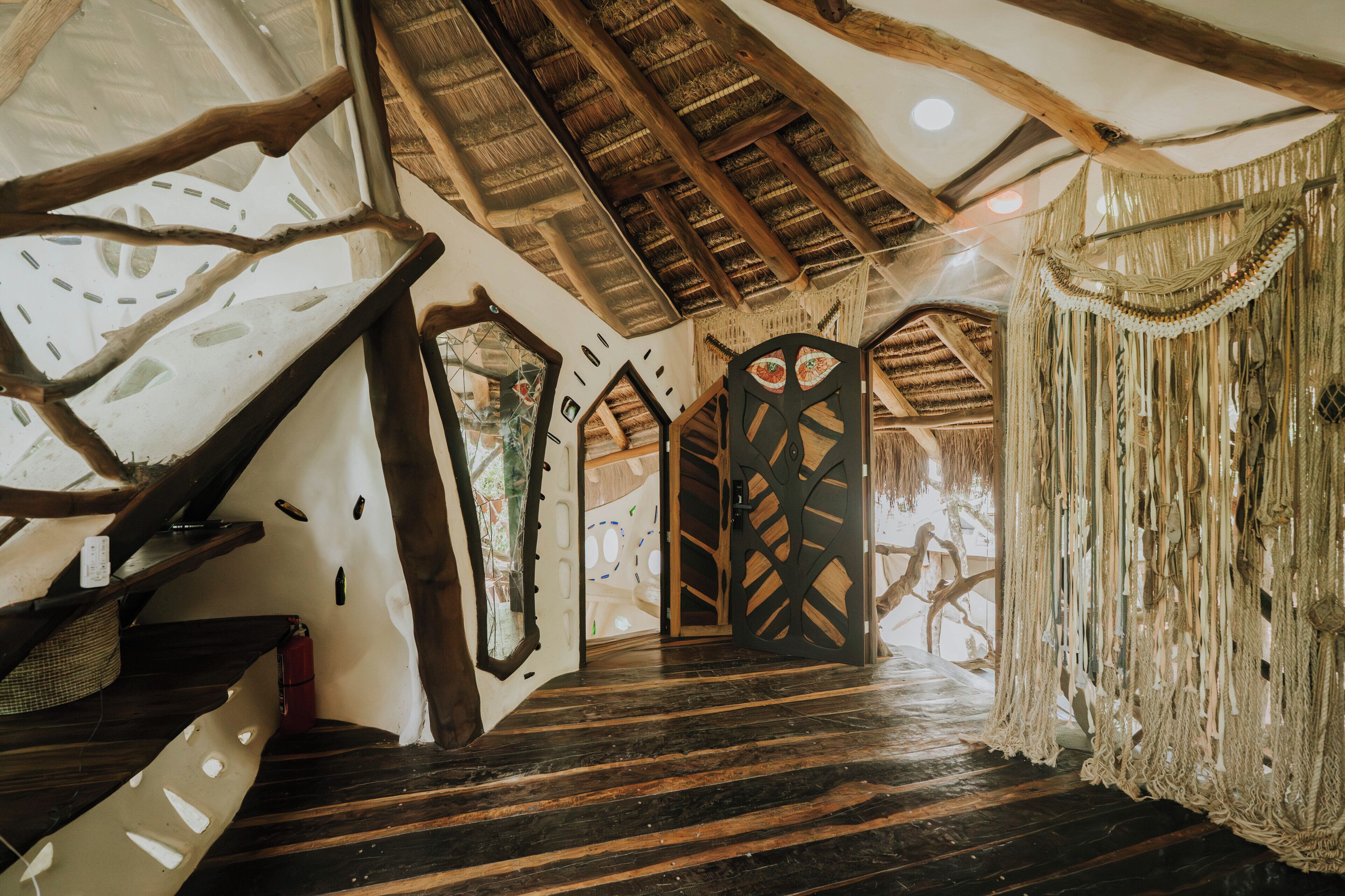 Een rustiek interieur met een houten trap, rieten dak en een opvallend deurbontwerp.