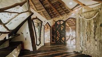 Een rustiek interieur met een houten trap, rieten dak en een opvallend deurbontwerp.
