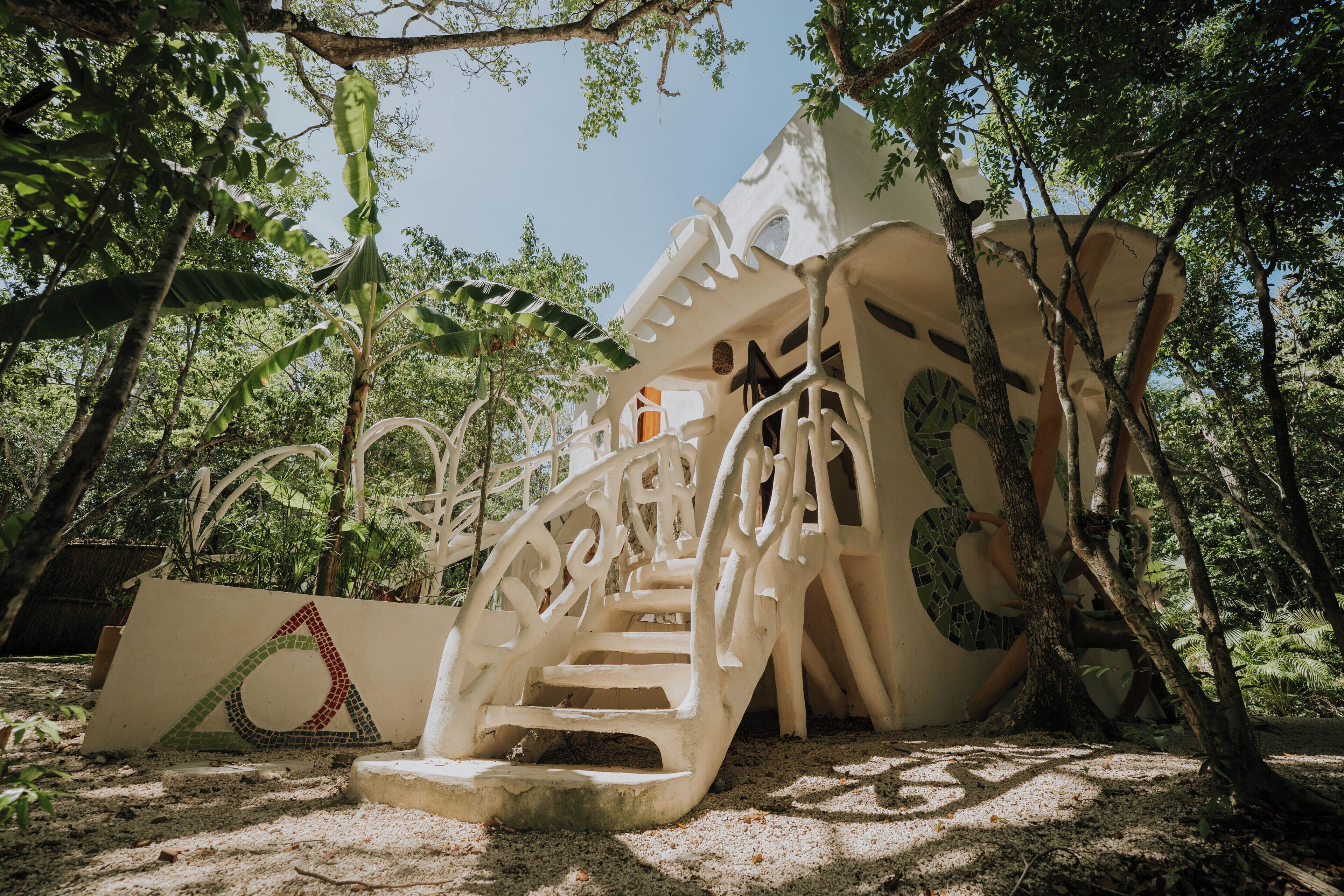 A white staircase with intricate designs leading up to a building, surrounded by lush greenery.