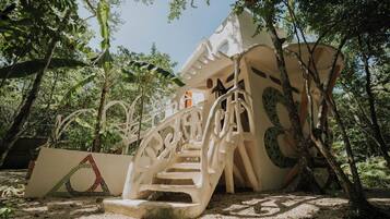 A white staircase with intricate designs leading up to a building, surrounded by lush greenery.