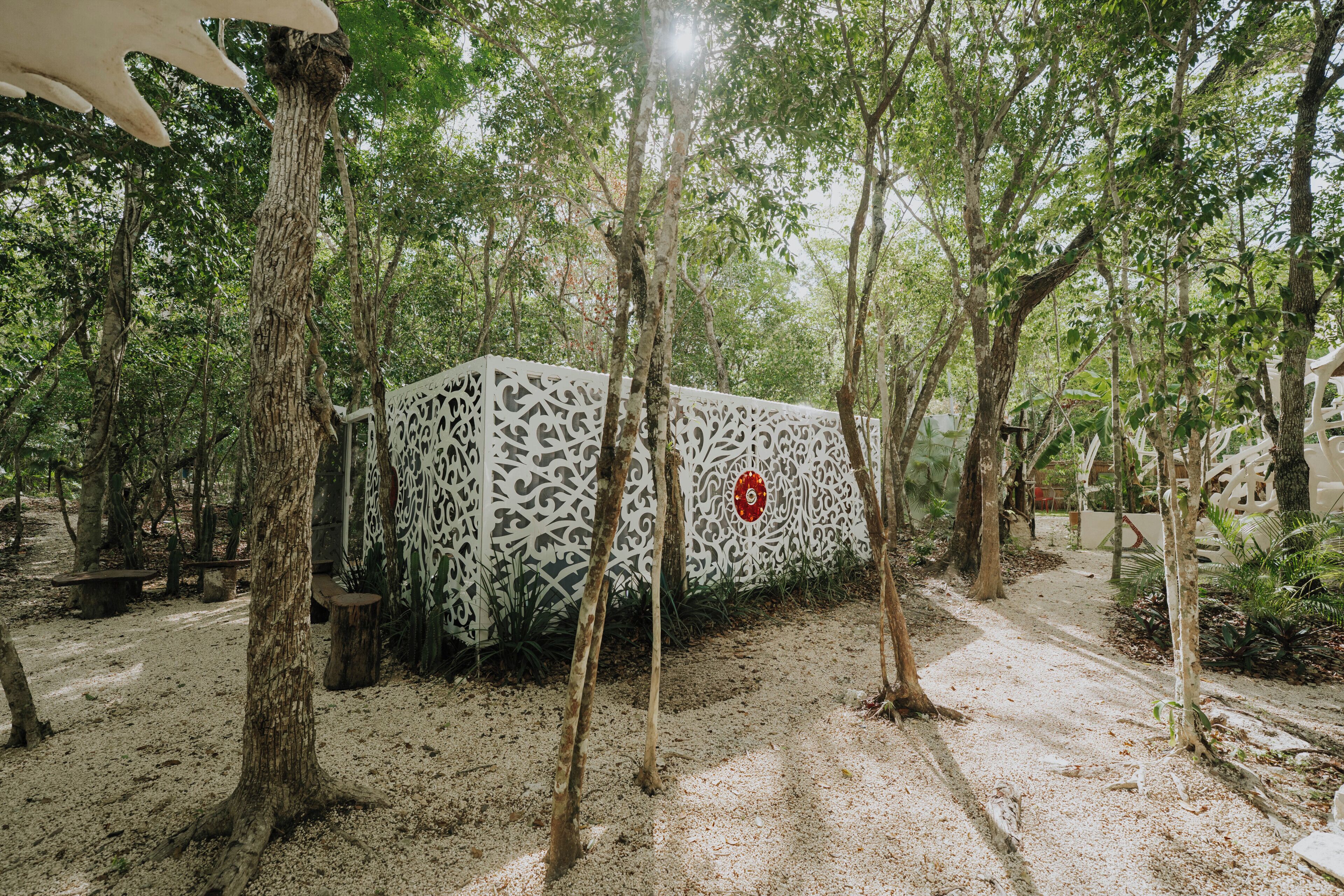 A pathway surrounded by trees and a decorative white fence with intricate patterns.