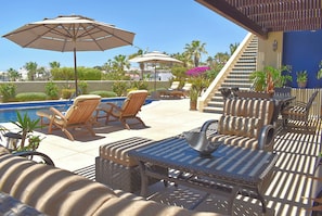 A poolside area with lounge chairs, umbrellas, and a staircase leading to an upper level.