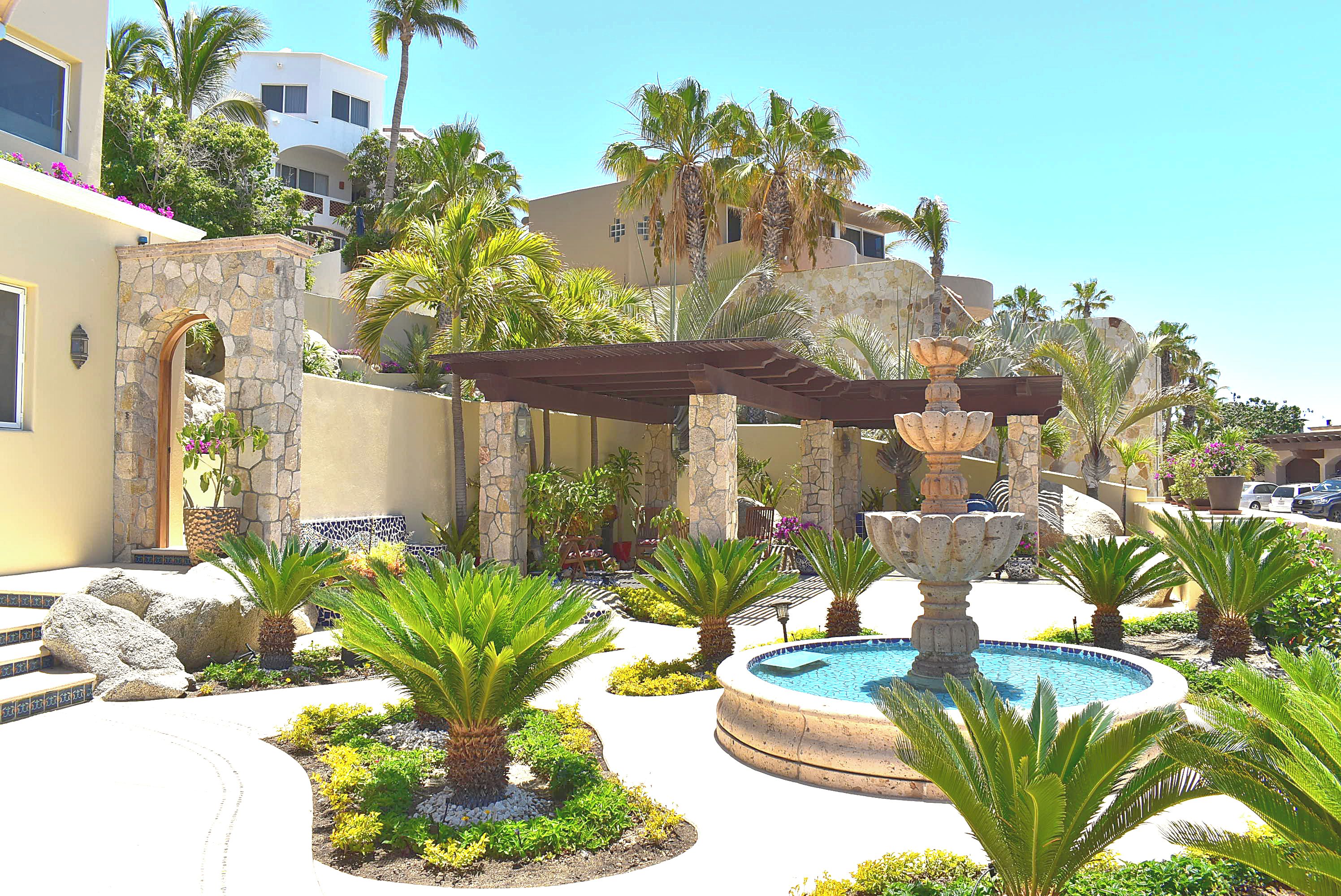 A pool area with a fountain, surrounded by palm trees and a stone wall.