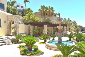 A pool area with a fountain, surrounded by palm trees and a stone wall.