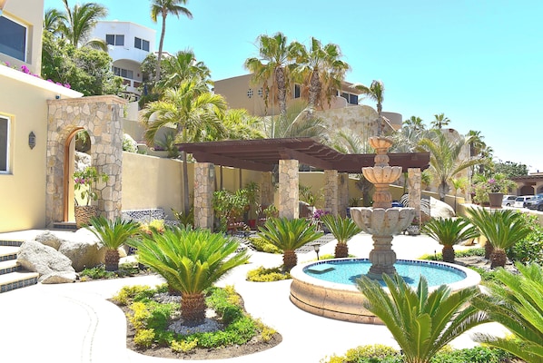 A pool area with a fountain, surrounded by palm trees and a stone wall.