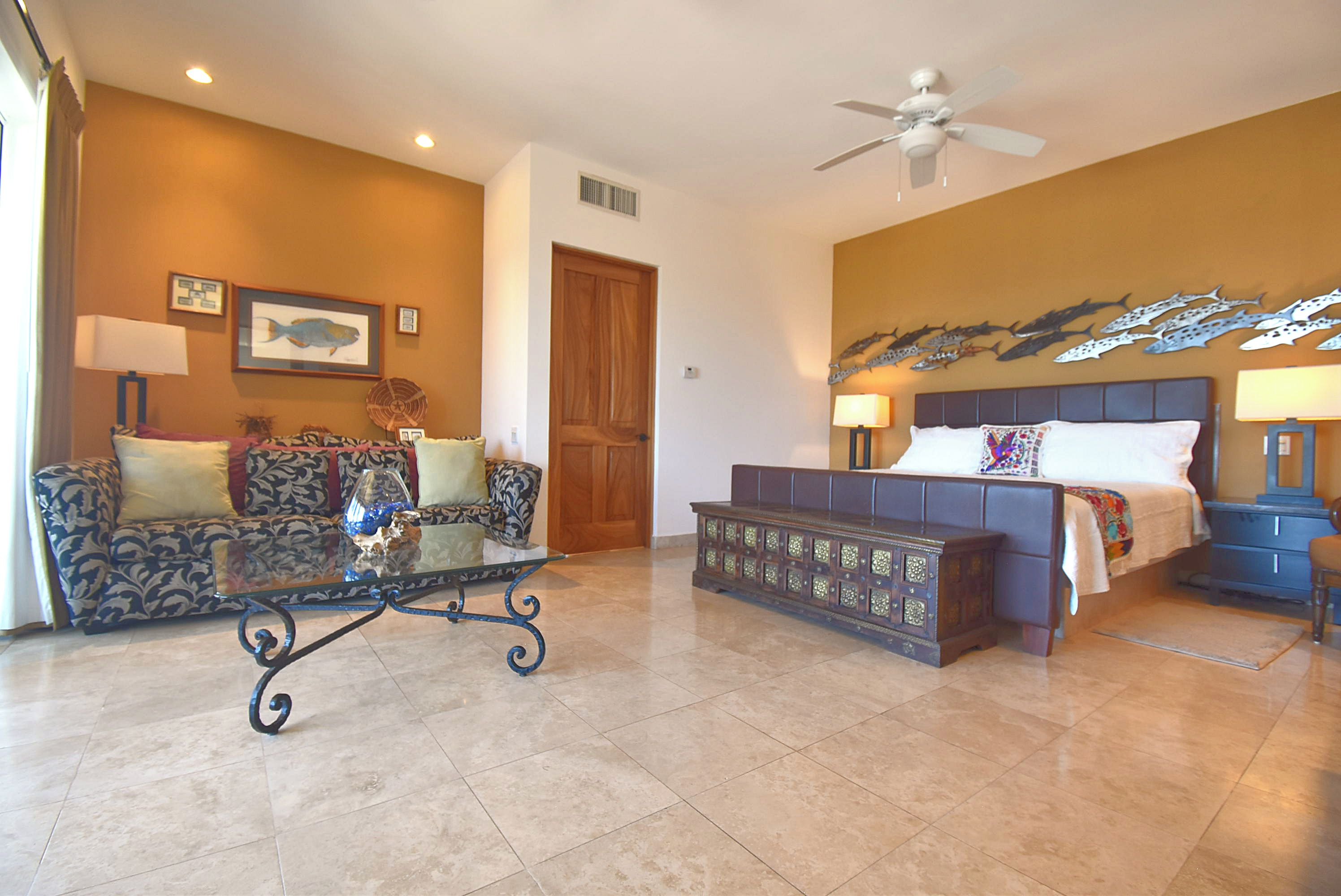 A hotel room with a bed, a sofa, a coffee table, and a ceiling fan.