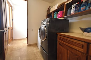A laundry area with a washing machine, wooden cabinets, and shelves with cleaning supplies.