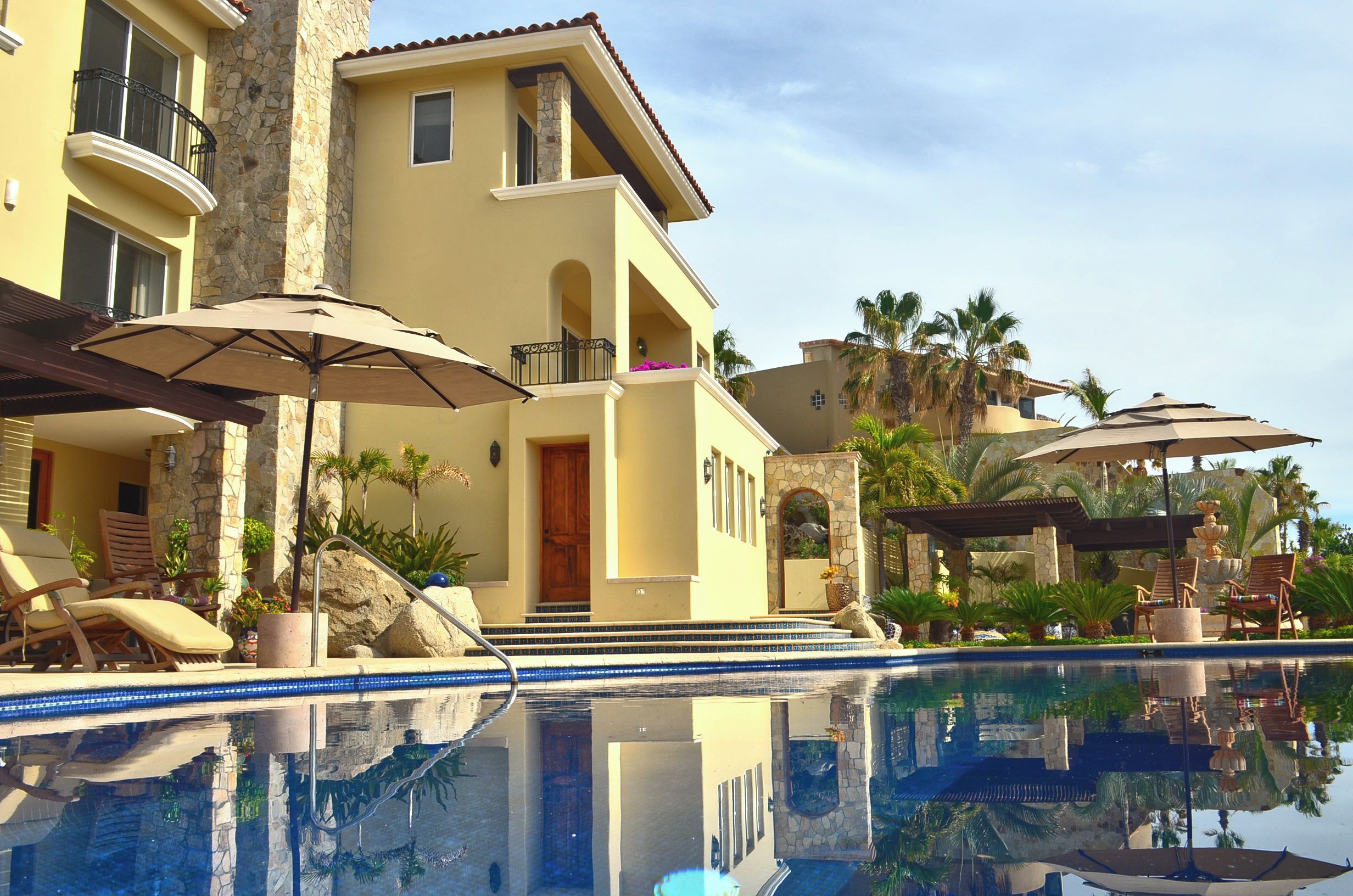 A two-story building with a pool, outdoor seating, and palm trees.