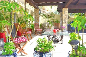 An outdoor patio area with wooden chairs, a glass table, and various potted plants.