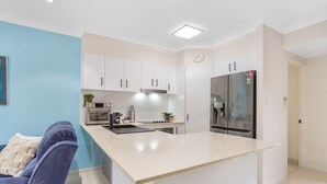 A modern kitchen with white cabinets, a stainless steel refrigerator, and a built-in island. - Nature View Southside Apartment (White Rock)