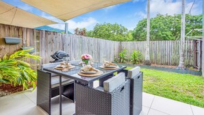 An outdoor patio with a table set for dining, surrounded by wicker furniture, a grill, and potted plants. - Nature View Southside Apartment (White Rock)