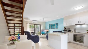 A modern kitchen with white cabinets, a built-in oven, and a dining area with a sofa and chairs. - Nature View Southside Apartment (White Rock)