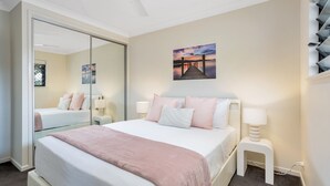 A bedroom with a large bed, a nightstand, a mirror, and a painting of a sunset over a pier. - Nature View Southside Apartment (White Rock)