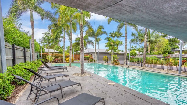 A swimming pool with lounge chairs, surrounded by palm trees and a covered area. - Nature View Southside Apartment (White Rock)