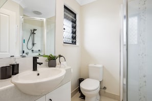 Un baño moderno con un lavabo grande, inodoro y ducha con mampara de vidrio.