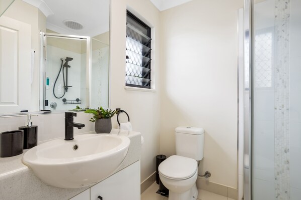 A modern bathroom with a large sink, toilet, and glass-enclosed shower.