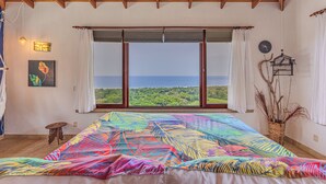 A bedroom with a large bed, a view of the sea, and a wooden ceiling.