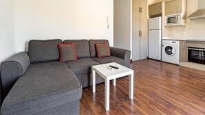 A modern living room with a grey sectional sofa, a white coffee table, and a kitchen area with a washing machine and microwave. - Luxury Apartments Puerto Valencia (Valencia)