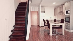 A modern kitchen with stainless steel appliances, a dining area with a wooden table and chairs, and a staircase with dark wood steps. - Luxury Apartments Puerto Valencia (Valencia)