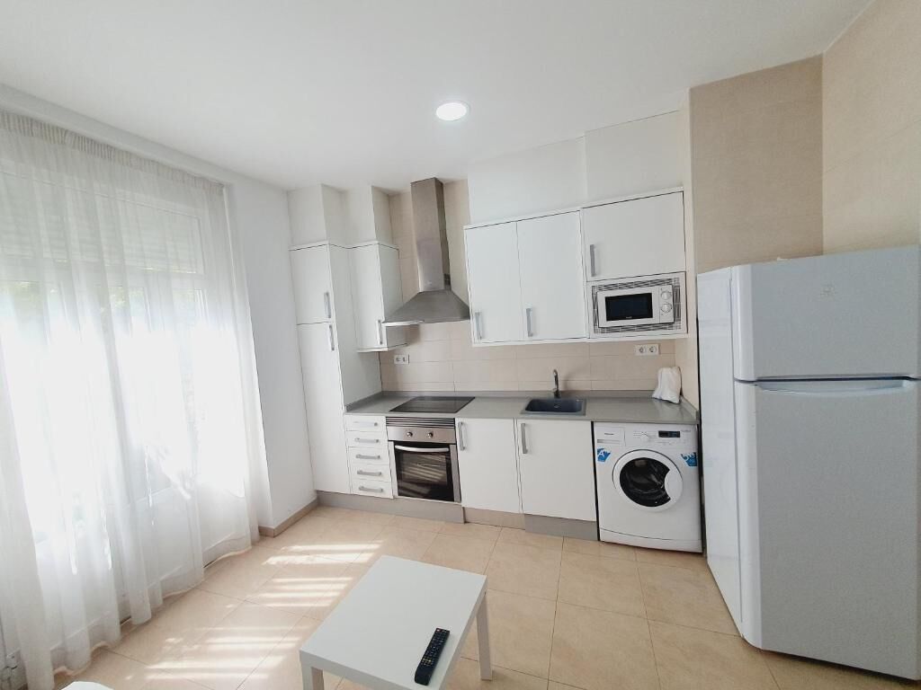 Una cocina moderna con armarios blancos, un microondas, una lavadora y un refrigerador.