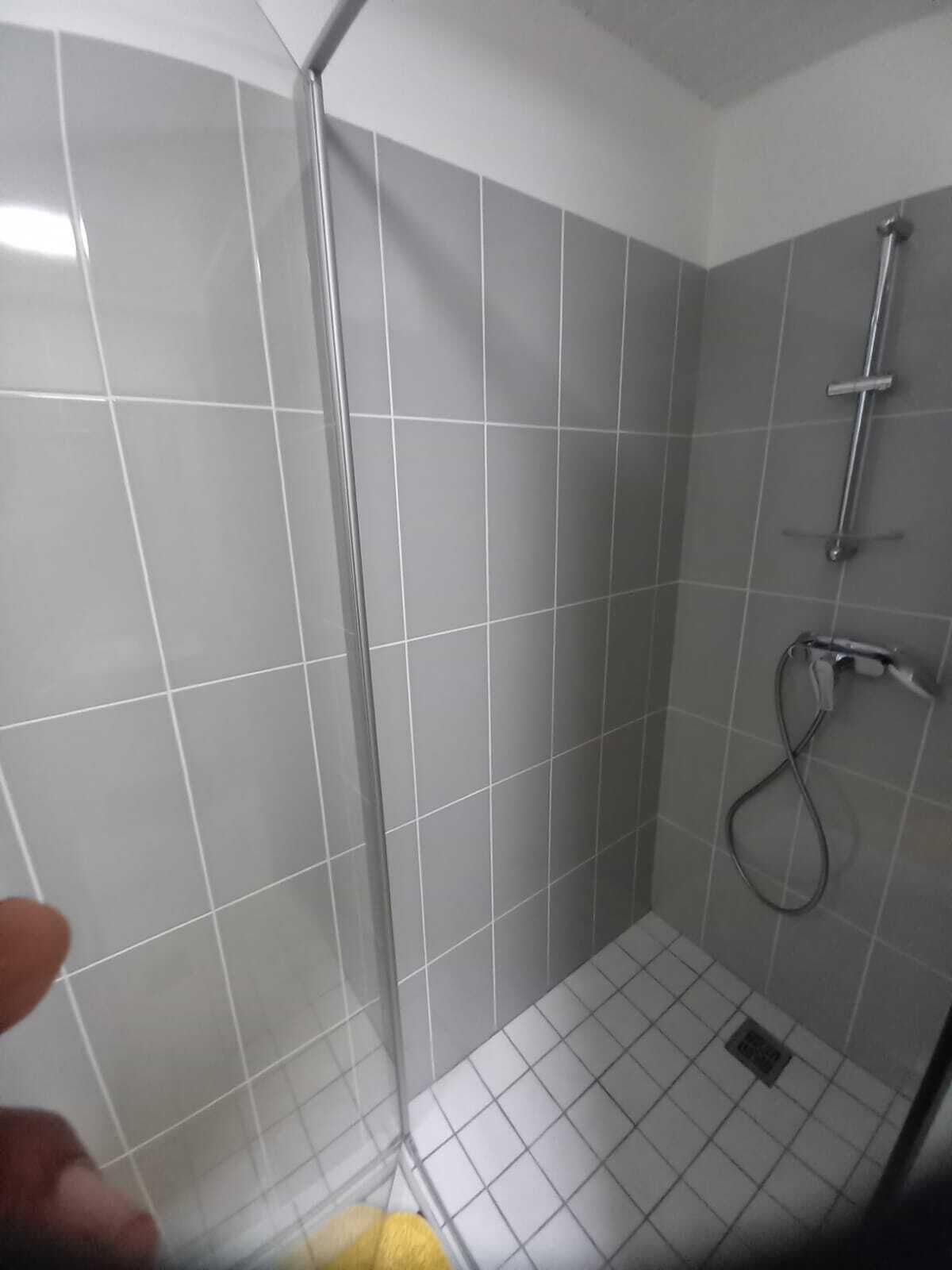A small, tiled shower room with a glass door and a handheld showerhead.