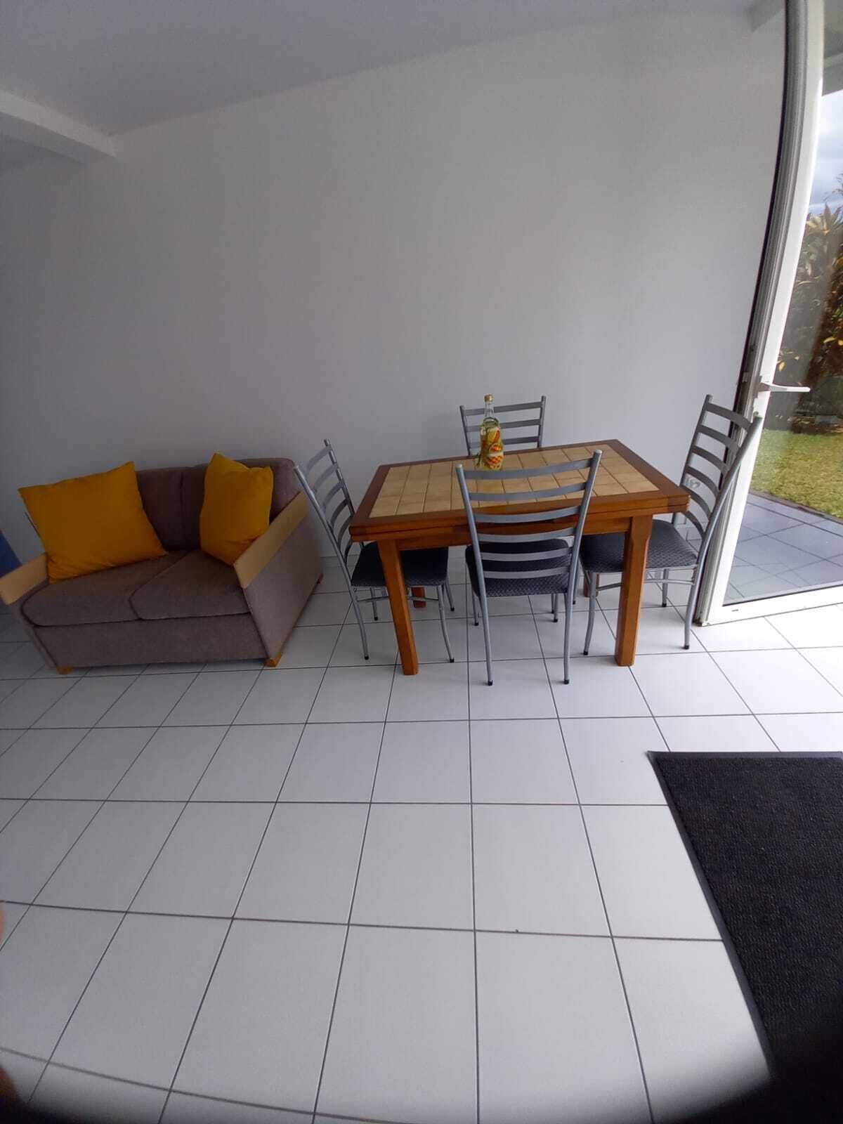 Een eetgedeelte met een tafel en stoelen, een bank met kussens en een glazen deur naar buiten.