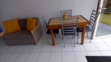 Een eetgedeelte met een tafel en stoelen, een bank met kussens en een glazen deur naar buiten.
