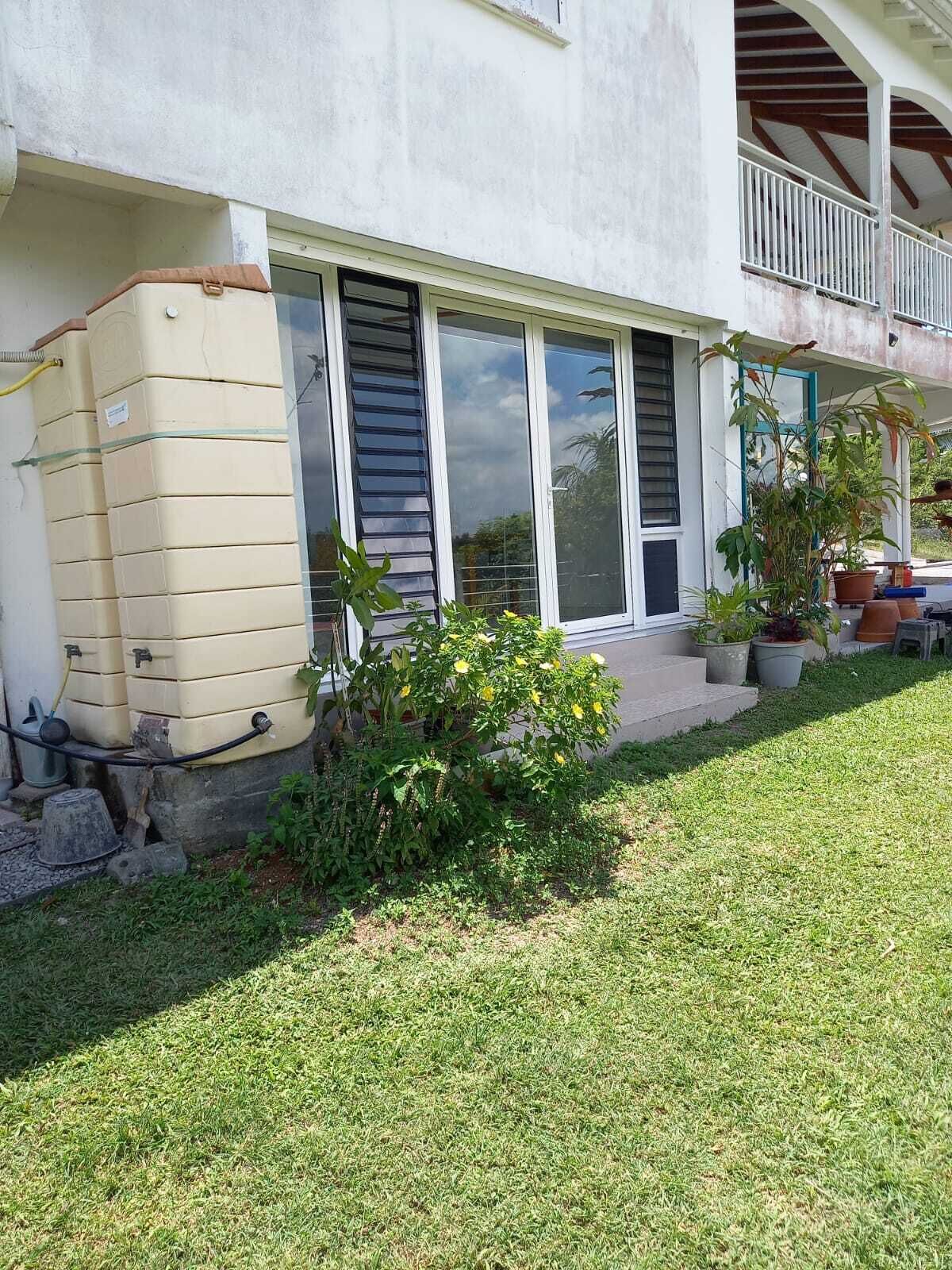 Ein Haus mit überdachter Veranda, einem Wassertank und einem kleinen Garten.