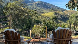 Two wooden Adirondack chairs with white fur trim facing a scenic view of rolling hills and a clear blue sky. - Cabana I nas Montanhas de Gonçalves (Gonçalves)