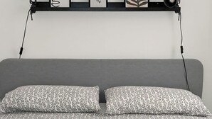A bed with patterned bedding, a headboard, and a shelf above with framed artwork and a lamp. - Nonna Jaca Apartament (Trapani)