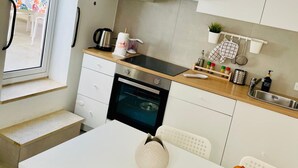 A modern kitchen with white cabinets, a stainless steel sink, and a built-in oven. There is a dining table with a vase of flowers and a chair. - Nonna Jaca Apartament (Trapani)