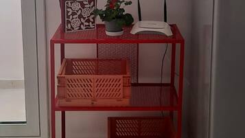 Une petite pièce avec une table en métal rouge sur laquelle sont posés une boîte décorative, une plante en pot et une horloge murale.