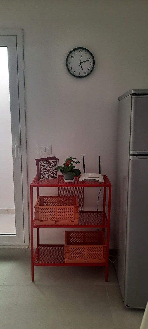 A small room with a red metal table holding a decorative box, a potted plant, and a clock on the wall.