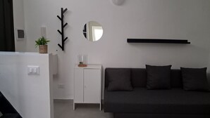 A modern living room with a dark grey sofa, a white cabinet with a plant, a black wall-mounted shelf, and a round mirror. - Nonna Jaca Apartament (Trapani)