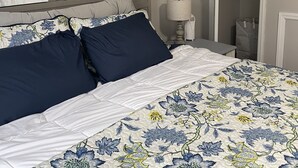 En pænt redt seng med et blomstret sengetæppe, to puder og to billeder af fugle hængt på væggen.