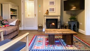 Un salon chaleureux avec une cheminée, un canapé, une table basse et un téléviseur à écran plat fixé au mur.
