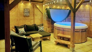 Une charmante cabane en bois avec un jacuzzi, un canapé agrémenté de coussins et une pancarte sur laquelle on peut lire : « LE BON VIEUX TEMPS ».