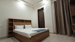 A bedroom with a wooden bed, white bedding, a nightstand, a wardrobe, and a curtain. - 85 The Ganges 2 Bhk Apartment for Homestay (Rishikesh)