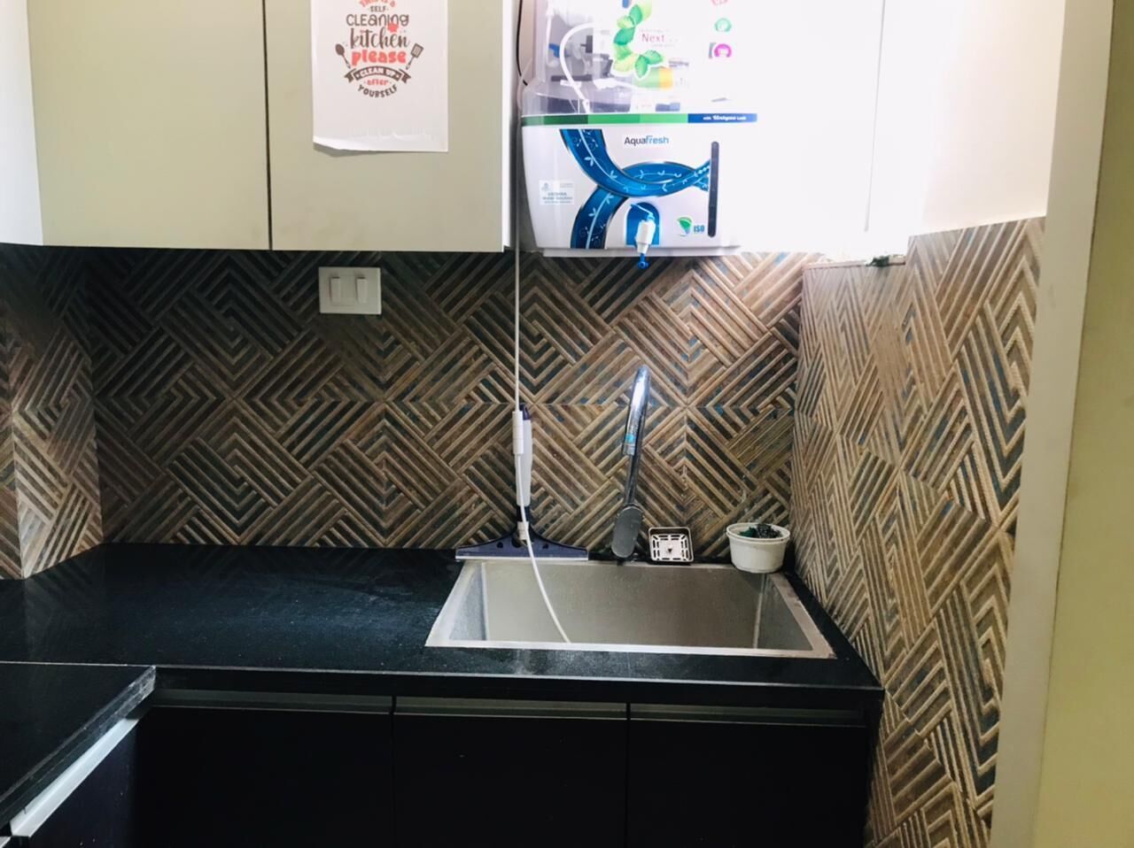 A kitchen with a sink, a faucet, a patterned backsplash, and a countertop.